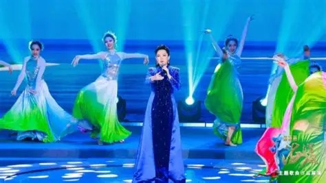 王庆爽身着蓝紫色礼服，站在舞台中央演唱