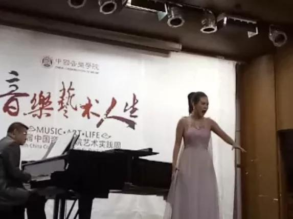 向安怡身着浅色礼服，在音乐厅演唱