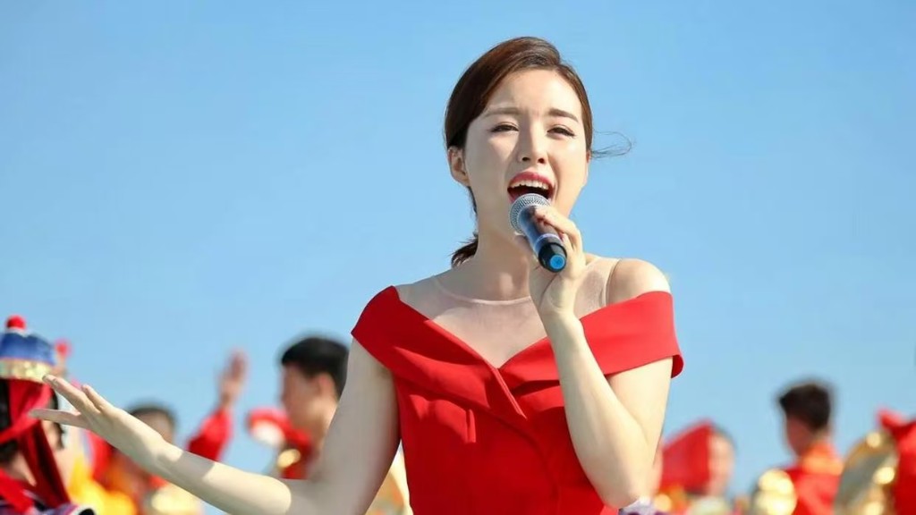 易文卉身着红色礼服，在户外舞台手持话筒演唱